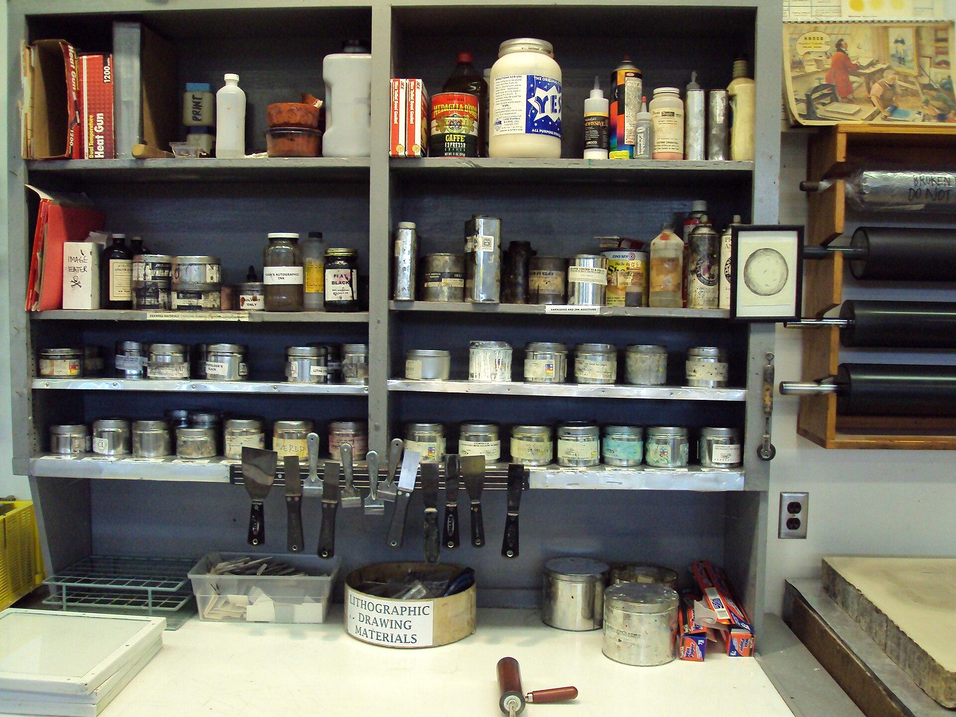 Shelves of printing inks in tins and jars above a workbench